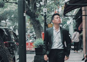 A fashionable young man in a suit strolling along a vibrant city street in Indonesia.